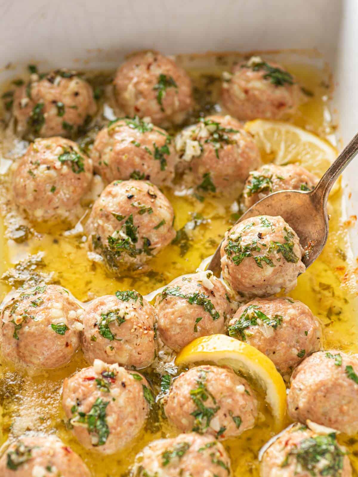 Garlic Butter Turkey Meatballs in a baking dish with a spoon scooping one.