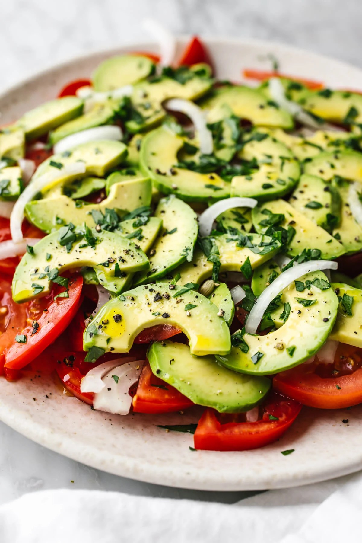 A large white plate of tomato, onion, and avocado salad