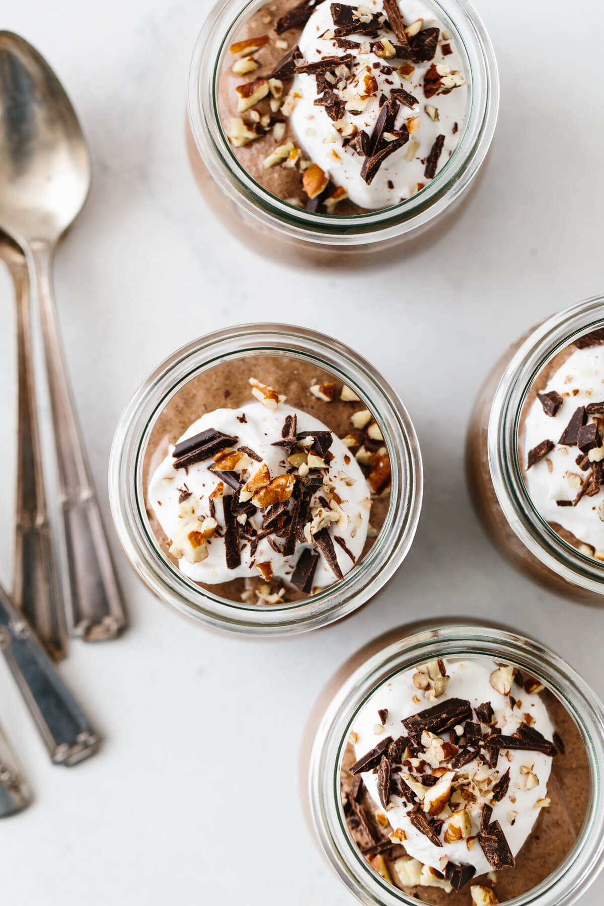 Four servings of chocolate chia mousse topped with coconut whipped cream, nuts and chocolate.