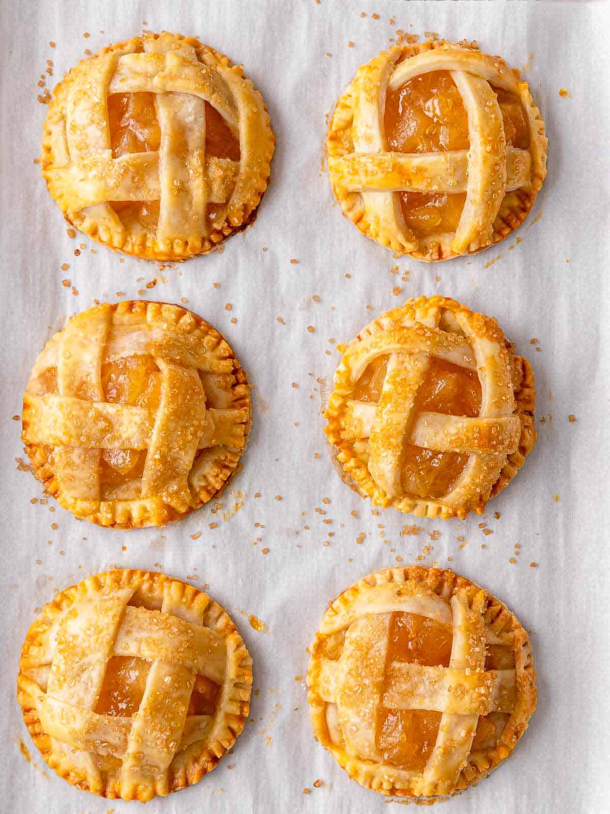 6 baked mini apple pies on a baking sheet pan after baking