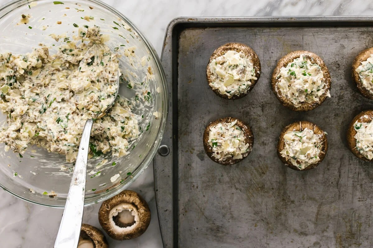 Stuffing mushrooms with filling on a sheet pan.