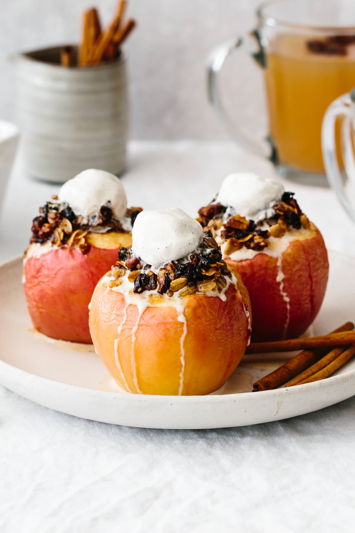 Three baked apples on a plate with melted ice cream on top.